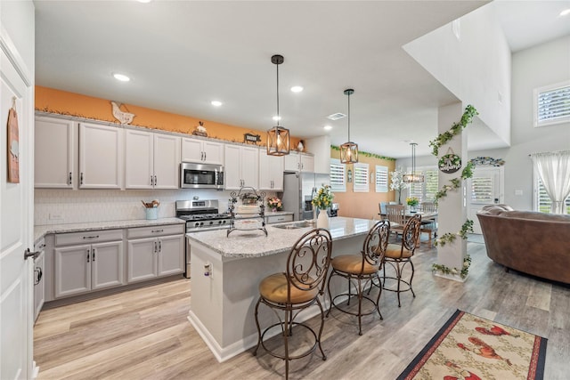 kitchen featuring light stone countertops, appliances with stainless steel finishes, a kitchen island with sink, pendant lighting, and a breakfast bar area