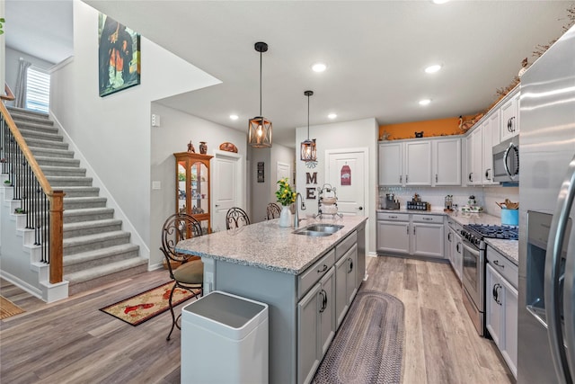 kitchen featuring light hardwood / wood-style floors, light stone countertops, appliances with stainless steel finishes, a kitchen island with sink, and sink