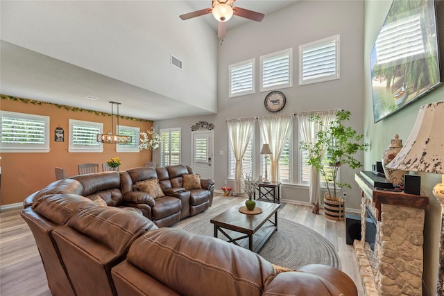 living room featuring ceiling fan with notable chandelier, light hardwood / wood-style flooring, and a towering ceiling