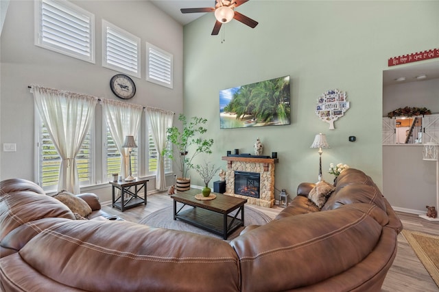 living room featuring a fireplace, light wood-type flooring, a high ceiling, and ceiling fan