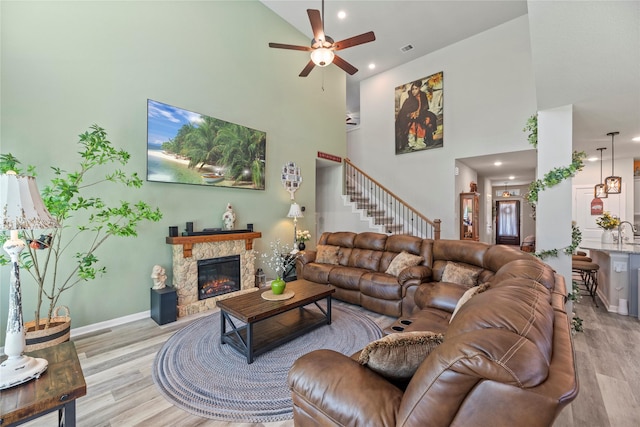 living room featuring ceiling fan, light wood-type flooring, a towering ceiling, and a stone fireplace