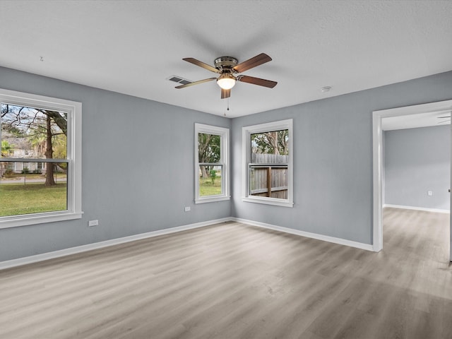 empty room featuring ceiling fan, light wood-type flooring, and a wealth of natural light