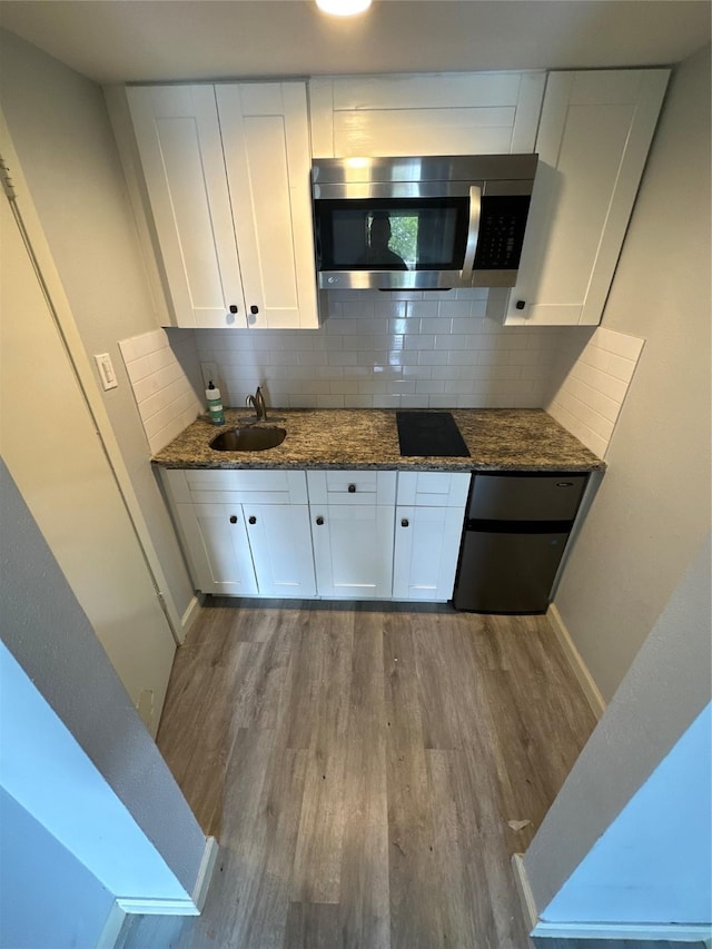 kitchen featuring sink, light wood-type flooring, white cabinetry, and dark stone counters