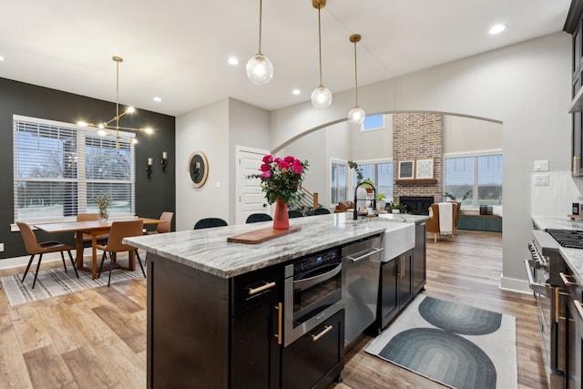 kitchen with a kitchen island with sink, appliances with stainless steel finishes, a sink, and decorative light fixtures