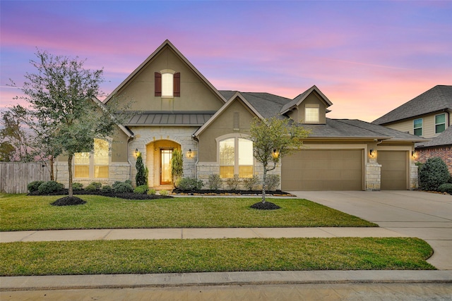 view of front of property featuring a yard, a standing seam roof, a garage, stone siding, and driveway