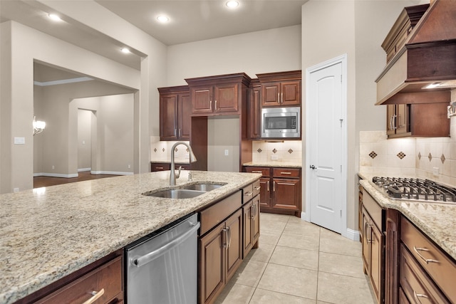 kitchen featuring appliances with stainless steel finishes, sink, premium range hood, light stone counters, and light tile patterned floors