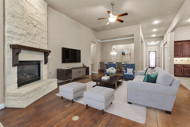 living room with ceiling fan with notable chandelier, light hardwood / wood-style flooring, and a stone fireplace