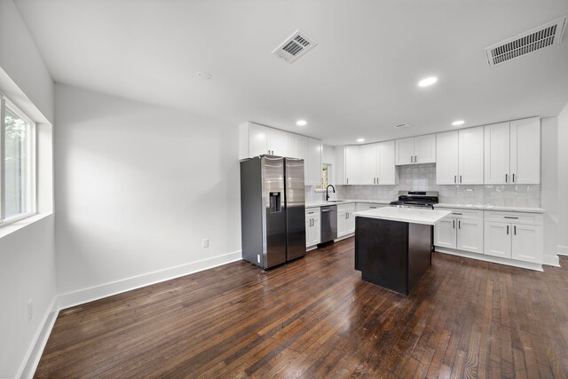 kitchen featuring appliances with stainless steel finishes, sink, white cabinets, a center island, and decorative backsplash