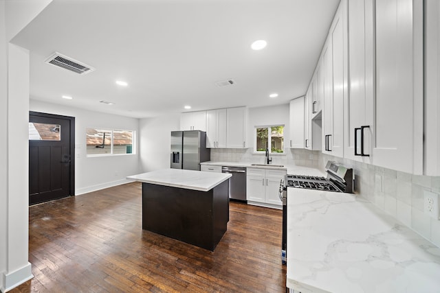 kitchen featuring white cabinets, appliances with stainless steel finishes, a kitchen island, tasteful backsplash, and light stone counters