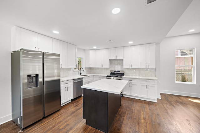 kitchen with appliances with stainless steel finishes, sink, white cabinetry, light stone countertops, and a center island