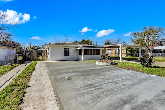 ranch-style home featuring a sunroom, a carport, driveway, and fence