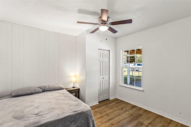 bedroom with a textured ceiling, wood finished floors, a closet, baseboards, and ceiling fan