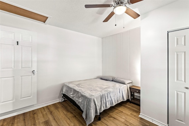 bedroom featuring a ceiling fan, wood finished floors, baseboards, and a textured ceiling