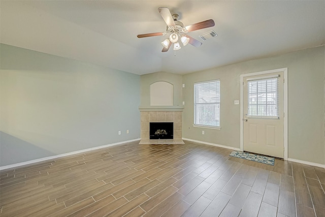 unfurnished living room featuring a tiled fireplace, wood-type flooring, and ceiling fan