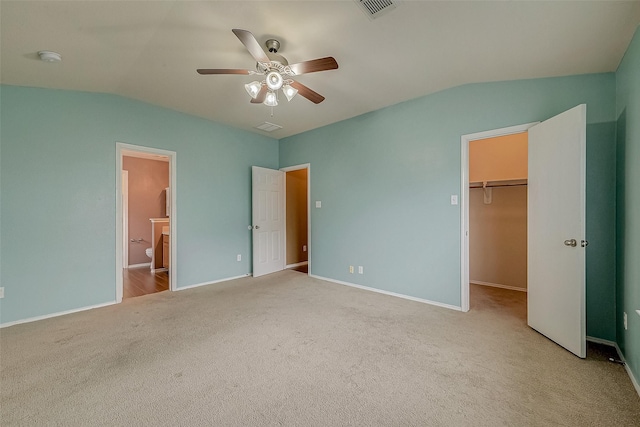 unfurnished bedroom featuring ensuite bathroom, a walk in closet, ceiling fan, light carpet, and a closet