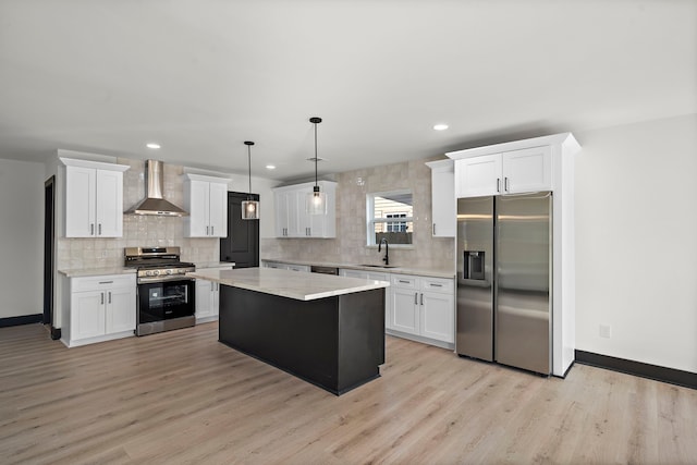 kitchen featuring wall chimney range hood, a kitchen island, sink, decorative light fixtures, and stainless steel appliances