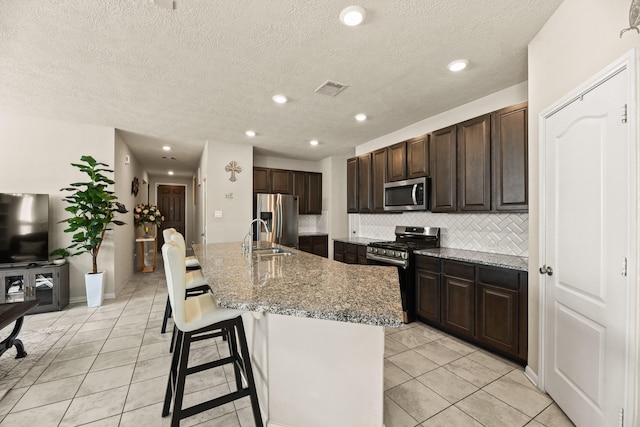 kitchen with appliances with stainless steel finishes, decorative backsplash, a kitchen breakfast bar, light tile patterned floors, and a center island with sink