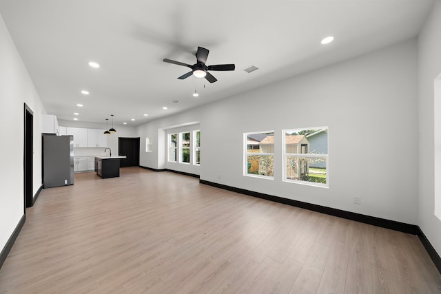 unfurnished living room featuring sink, light hardwood / wood-style floors, and ceiling fan