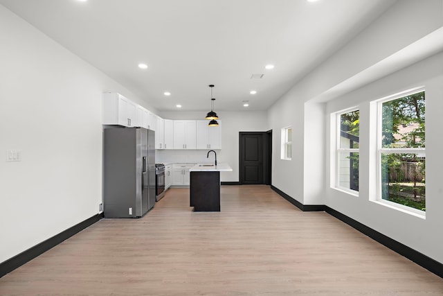 kitchen with light hardwood / wood-style floors, a kitchen island with sink, white cabinets, pendant lighting, and stainless steel appliances