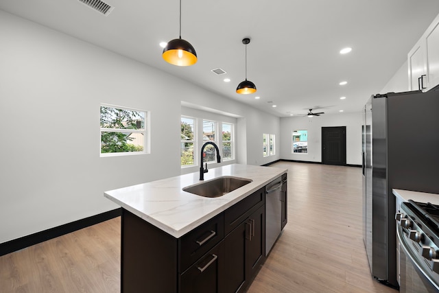 kitchen with decorative light fixtures, stainless steel appliances, sink, a kitchen island with sink, and light hardwood / wood-style flooring