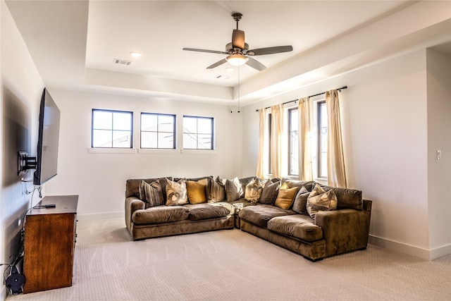 carpeted living room with a raised ceiling and ceiling fan