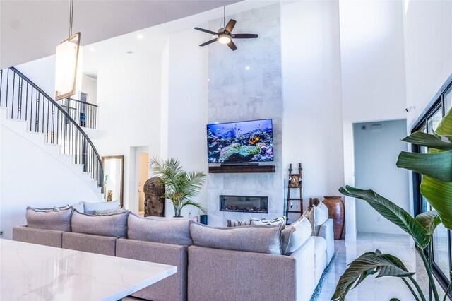 living room with a tiled fireplace, a high ceiling, and ceiling fan