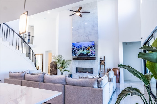 living room featuring a tiled fireplace, ceiling fan, and a high ceiling