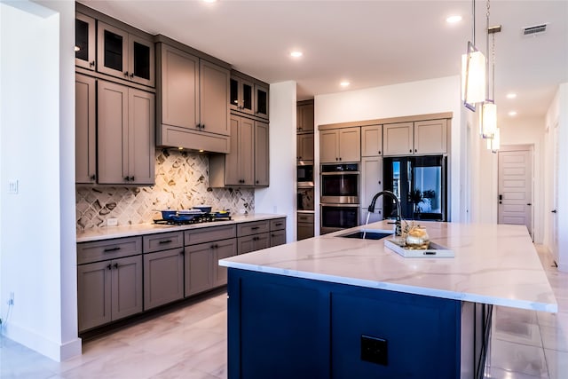 kitchen with a spacious island, appliances with stainless steel finishes, sink, decorative light fixtures, and light stone countertops