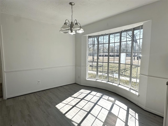 spare room featuring an inviting chandelier, plenty of natural light, dark hardwood / wood-style flooring, and a textured ceiling