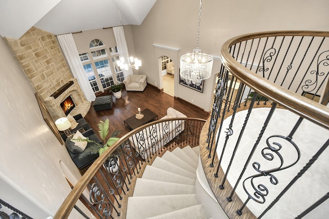 staircase featuring a notable chandelier, a stone fireplace, hardwood / wood-style floors, and a high ceiling