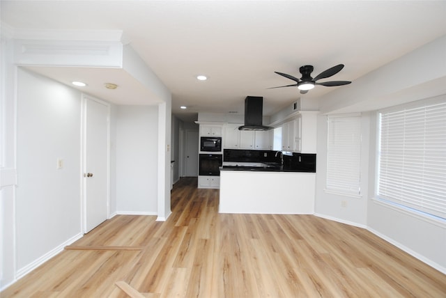 kitchen with white cabinets, black microwave, island exhaust hood, tasteful backsplash, and light hardwood / wood-style flooring