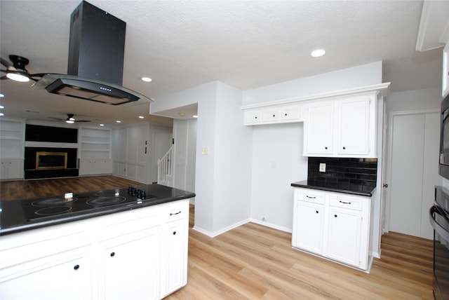 kitchen with black appliances, white cabinetry, island exhaust hood, decorative backsplash, and ceiling fan