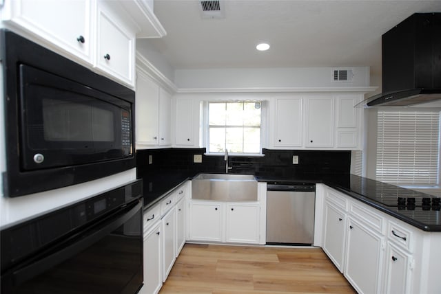 kitchen featuring black appliances, light wood-type flooring, wall chimney range hood, white cabinets, and sink