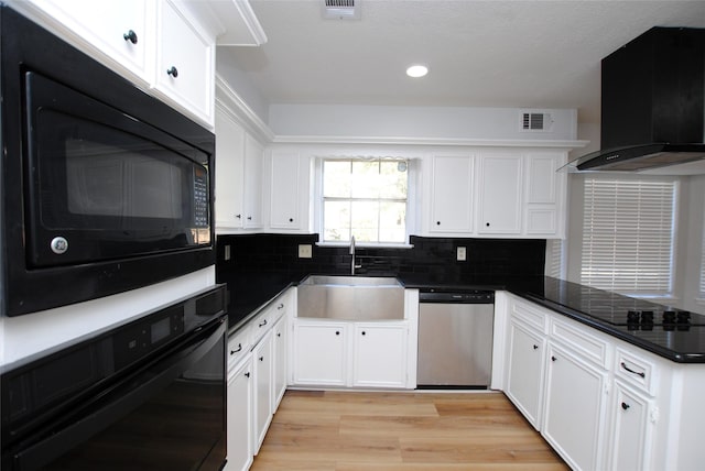 kitchen featuring black appliances, light wood-type flooring, white cabinets, sink, and wall chimney exhaust hood