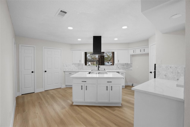 kitchen with light wood-type flooring, visible vents, island exhaust hood, white cabinets, and decorative backsplash