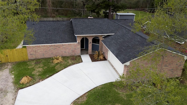 exterior space with fence, brick siding, and a shingled roof