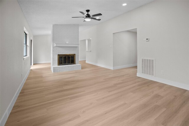 unfurnished living room featuring a brick fireplace, visible vents, light wood finished floors, and ceiling fan