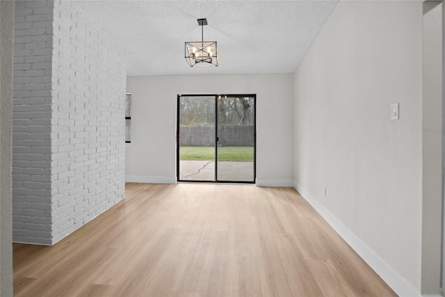 empty room featuring a chandelier, light wood-style flooring, a textured ceiling, and baseboards