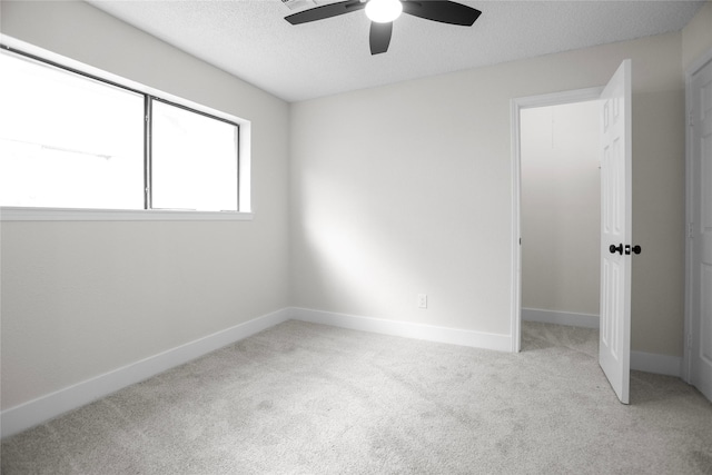 unfurnished bedroom featuring light carpet, a textured ceiling, baseboards, and a ceiling fan