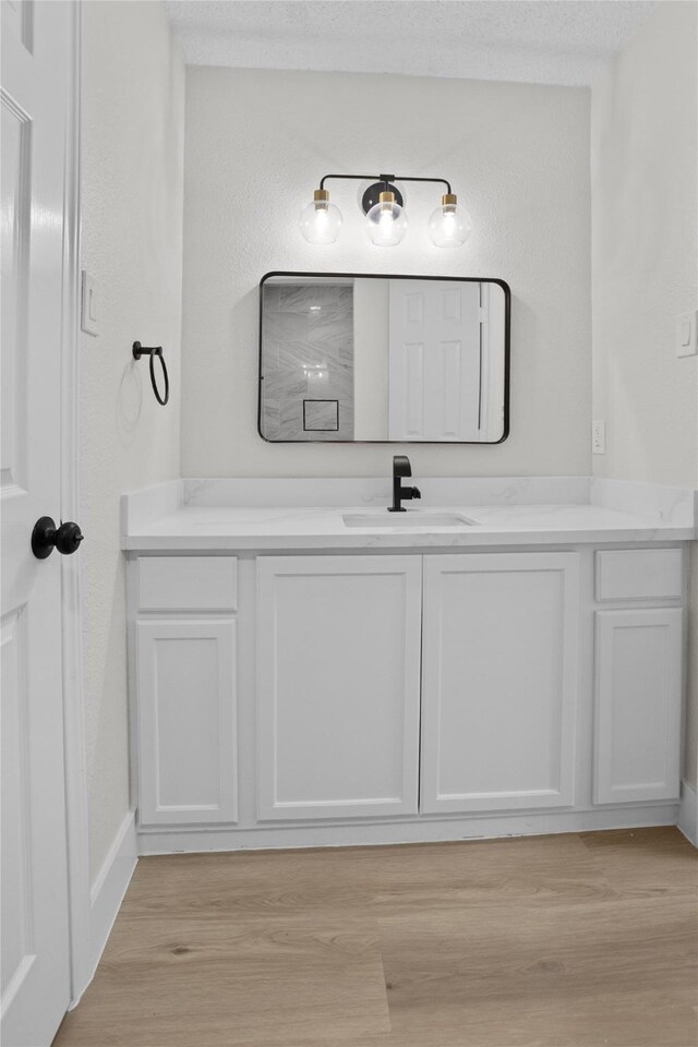 bathroom featuring a textured ceiling, wood finished floors, baseboards, vanity, and a textured wall