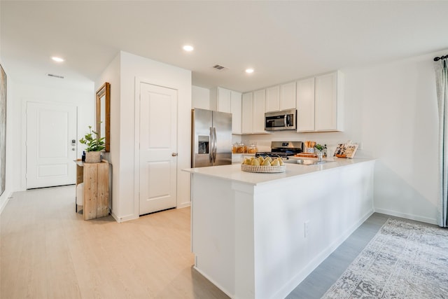 kitchen featuring kitchen peninsula, white cabinets, light hardwood / wood-style flooring, and stainless steel appliances