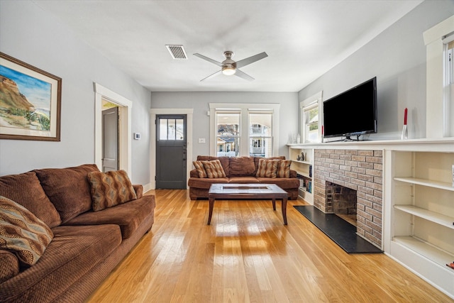 living room featuring ceiling fan, a fireplace, light hardwood / wood-style floors, and built in features