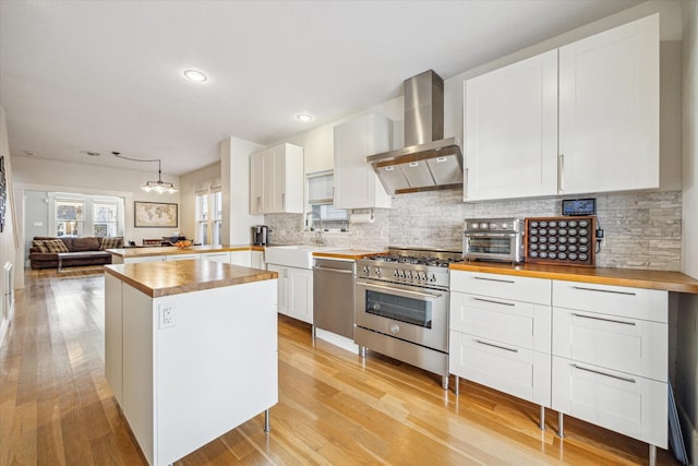 kitchen with sink, light hardwood / wood-style flooring, appliances with stainless steel finishes, wall chimney range hood, and white cabinets