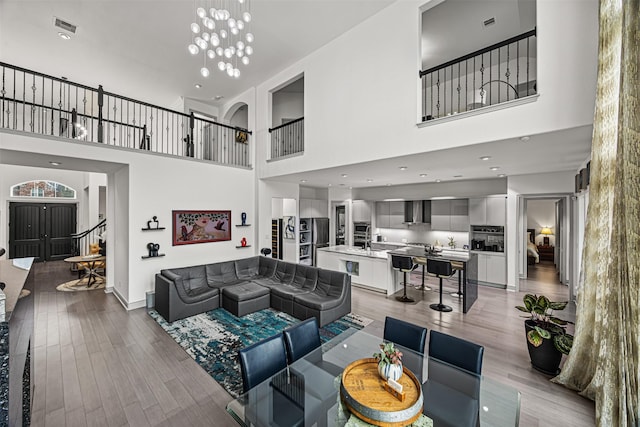 living room featuring light wood-type flooring, a chandelier, and a towering ceiling