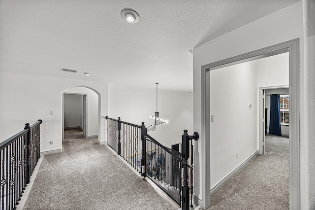 hall with carpet floors, a textured ceiling, and an inviting chandelier