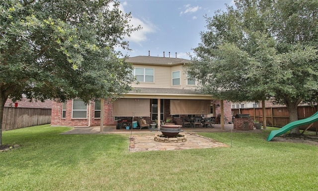 back of property with a playground, an outdoor fire pit, a lawn, and a patio