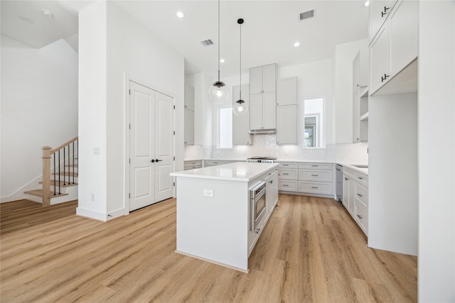 kitchen featuring white cabinetry, decorative light fixtures, a kitchen island, stainless steel appliances, and light hardwood / wood-style floors