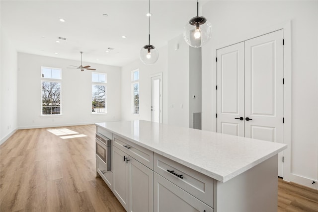 kitchen featuring a kitchen island, stainless steel microwave, white cabinets, hanging light fixtures, and light wood-type flooring