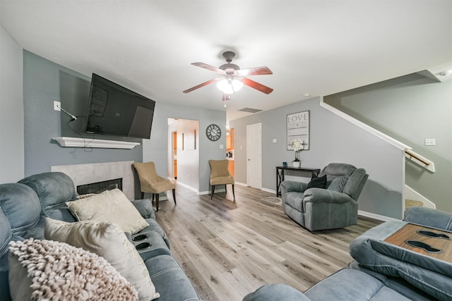 living room featuring light wood-type flooring, ceiling fan, and a fireplace