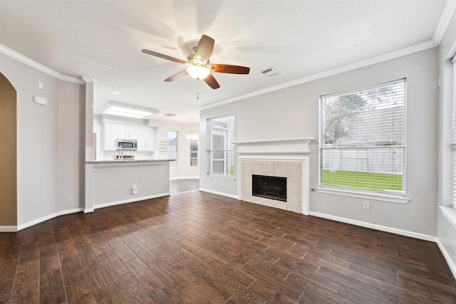 unfurnished living room featuring a tile fireplace, ornamental molding, dark hardwood / wood-style floors, and ceiling fan